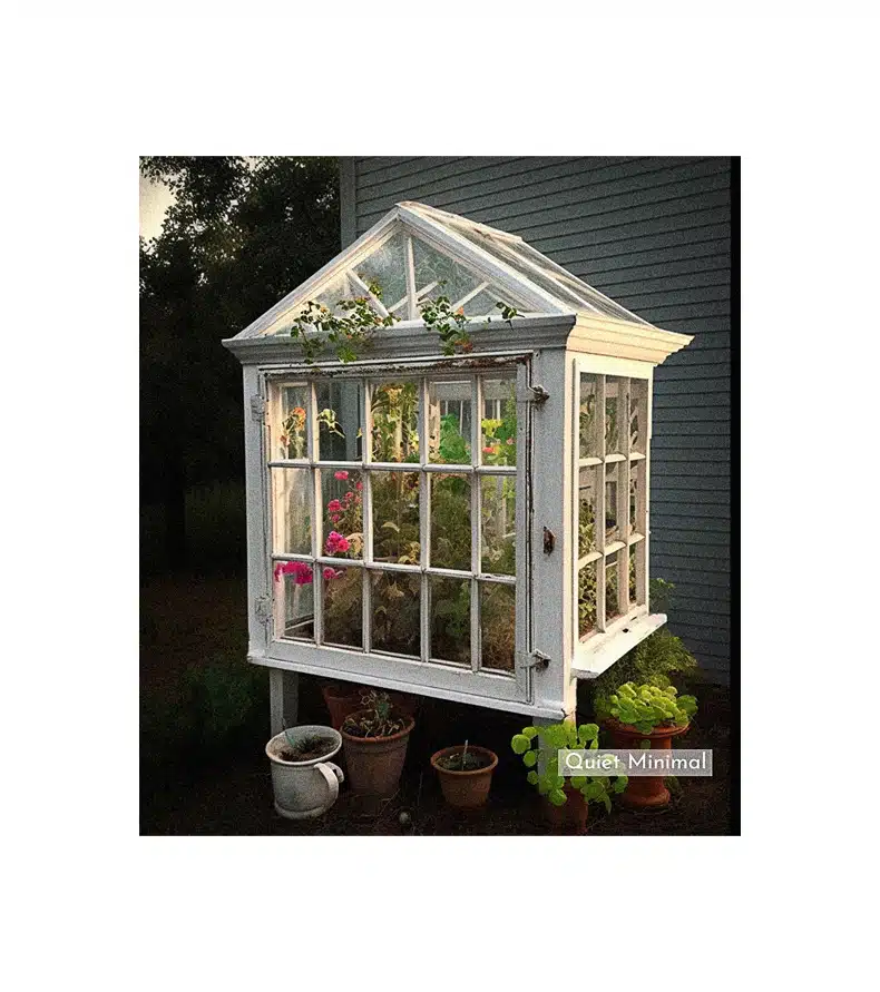 A repurposed greenhouse with potted plants, utilizing old vintage windows.