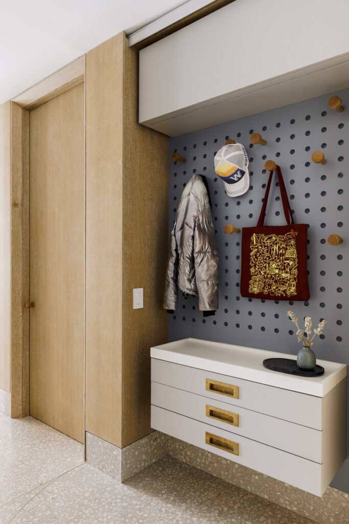 A hallway with a coat rack and a bag hanging on a pegboard.