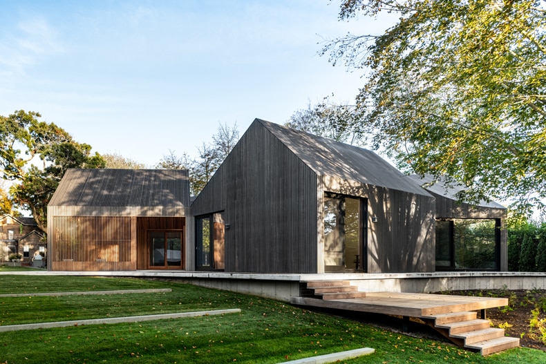 A modern wooden house sits on a grassy hillside.