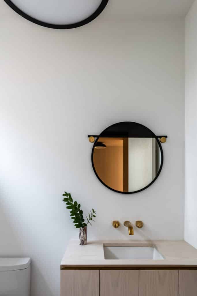 A bathroom with a round mirror and wooden vanity.