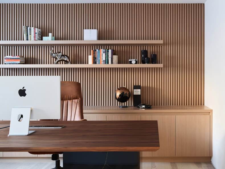 A modern home office with a wooden desk and shelves fashion by BLA Design Group.