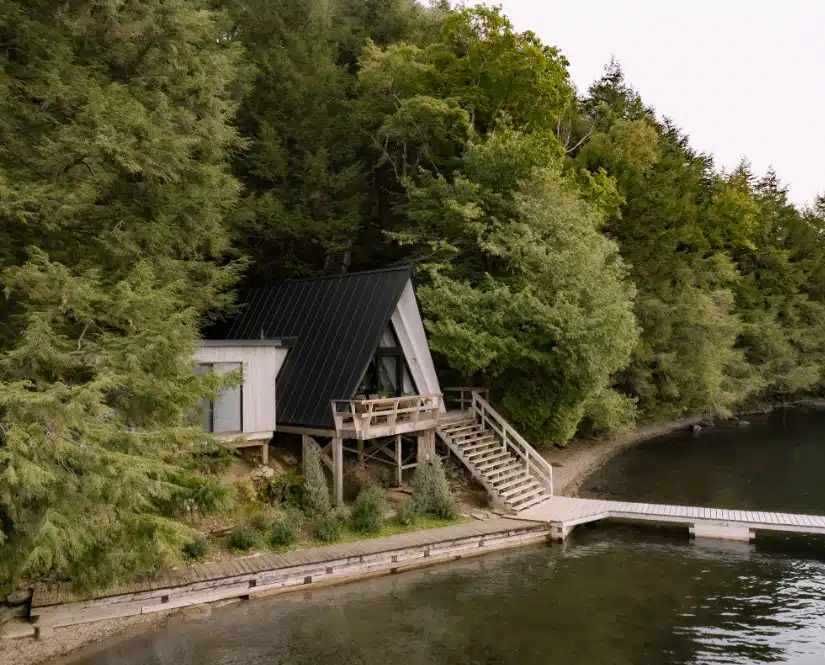 A small chalet sits on a dock next to a body of water.