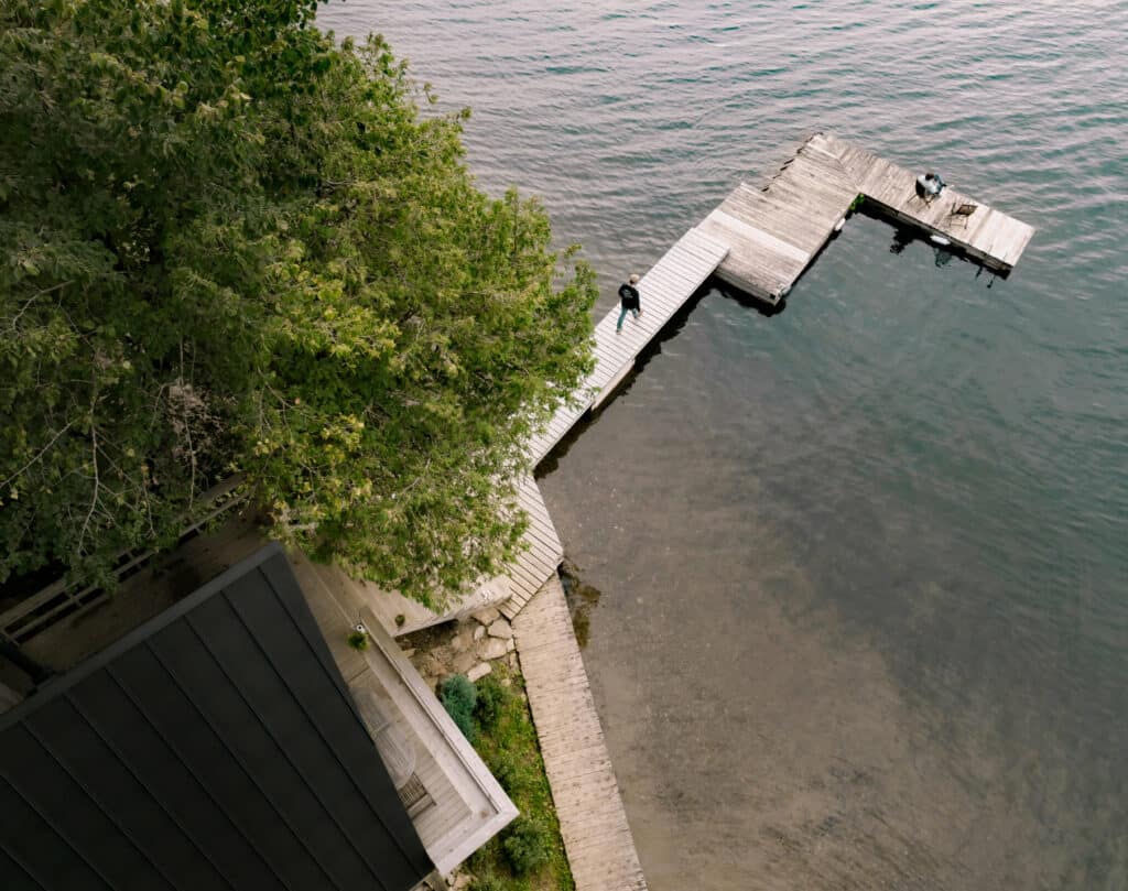 An aerial view of a dock on a serene lake surrounded by chalet-inspired architecture.