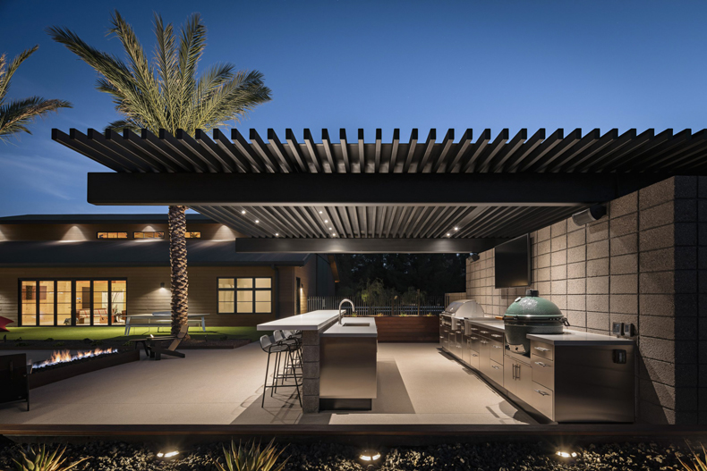 A modern outdoor kitchen with a fire pit and palm trees.