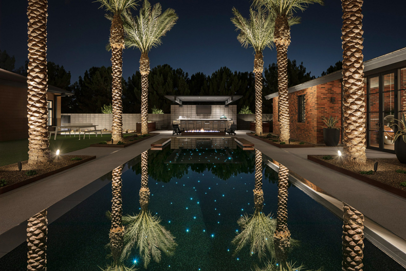 A backyard with palm trees and a pool at night.