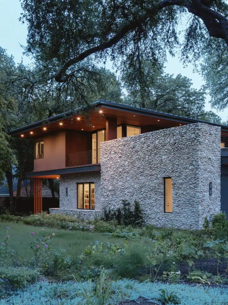 A modern house with a stone wall and trees.