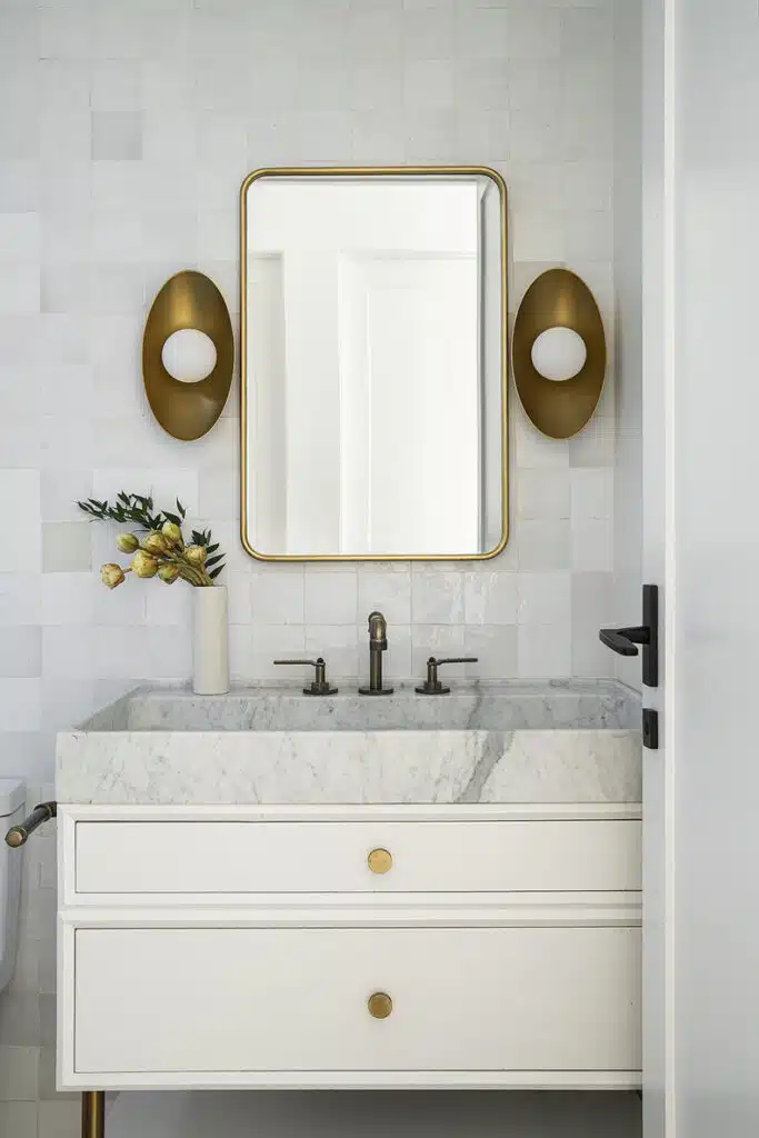 A white bathroom with gold accents and a mirror.