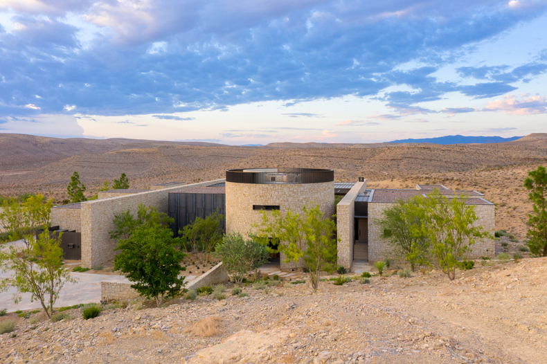A modern house sits on top of a hill in the desert.