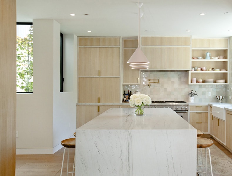 A modern kitchen with marble counter tops and wooden stools.