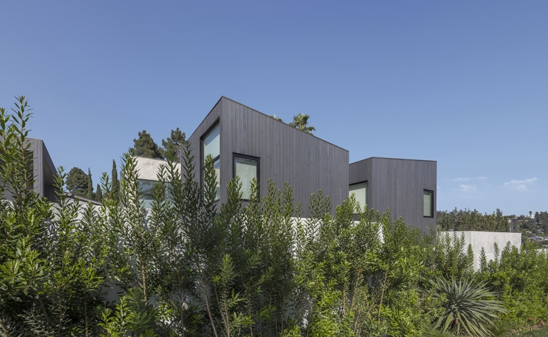 A modern house surrounded by bushes and trees.