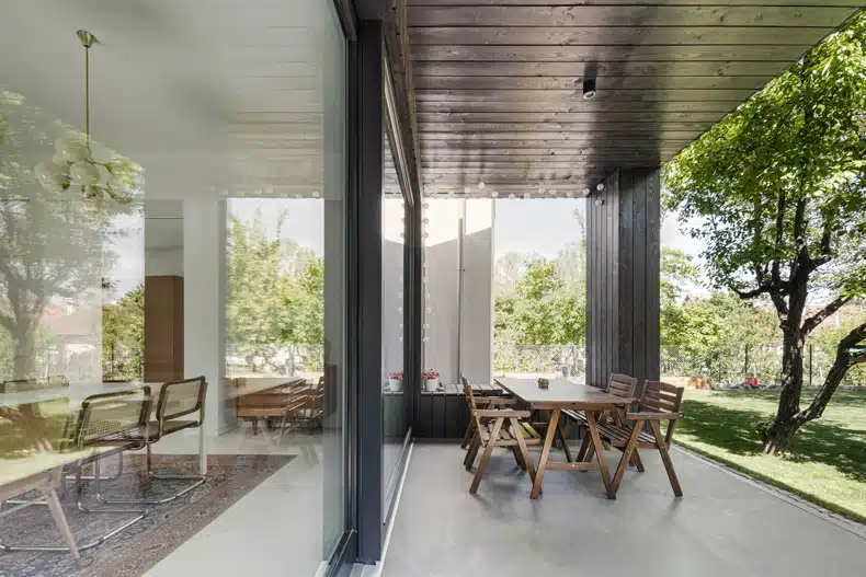 An outdoor dining area with glass walls and a wooden table.