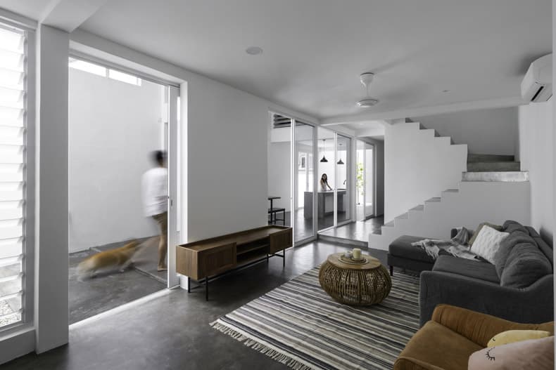 A white living room with stairs and a dog, showcasing the splendors of Insight House by Core Design Workshop.