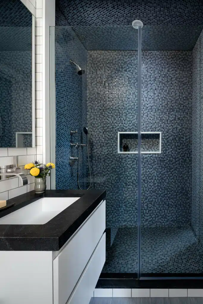 A bathroom with a glass shower stall and black counter top.