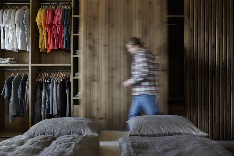A man walking through a bedroom with a closet full of clothes.