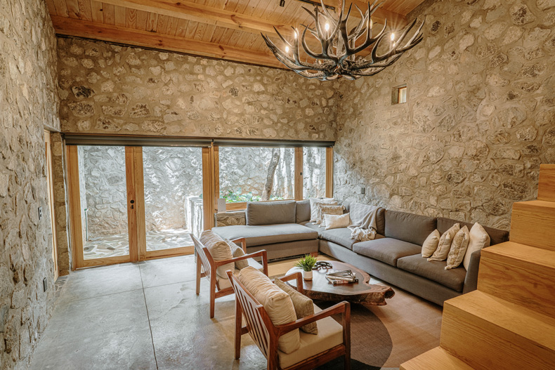 Petraia House By Argdl, a living room with stone walls and a chandelier.