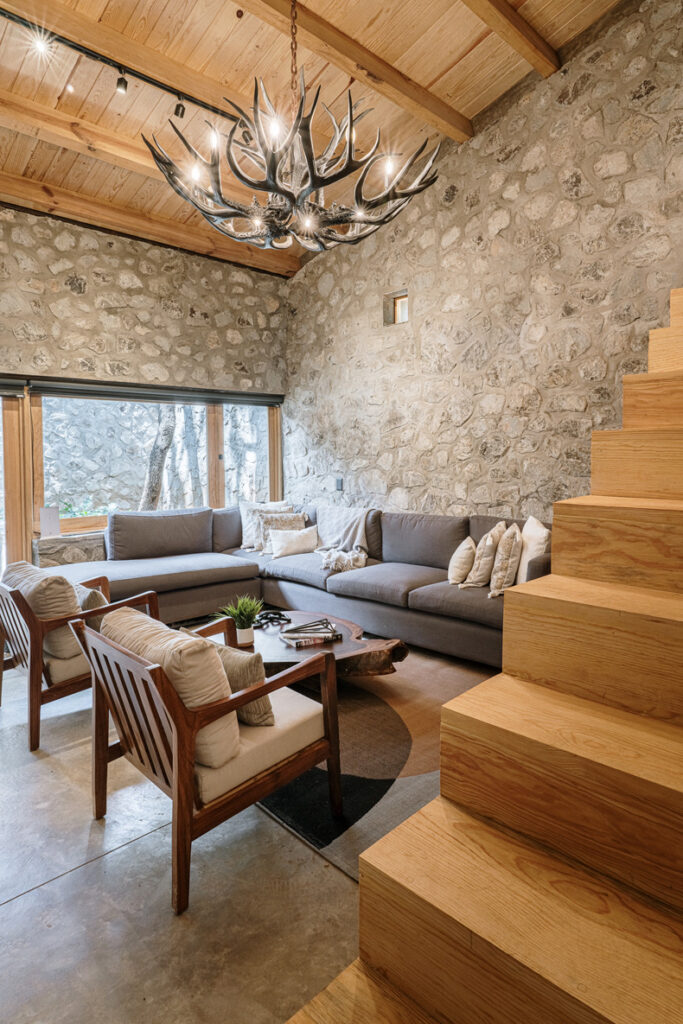 Petraia House by Argdl features a living room adorned with a stone wall and wooden stairs.