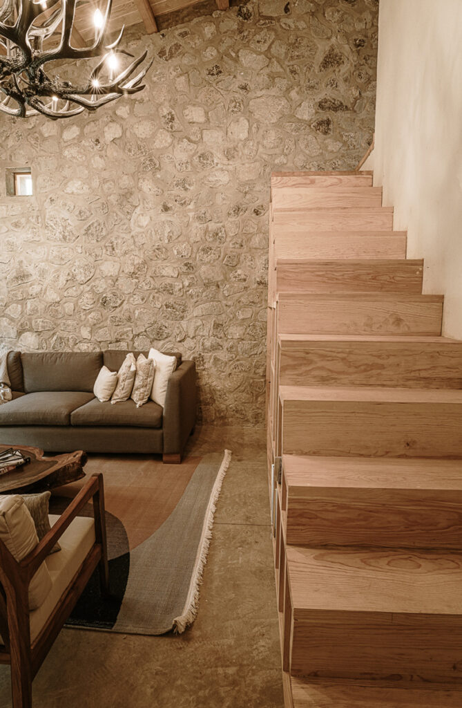 A living room in the Petraia House featuring a stone wall and wooden stairs.