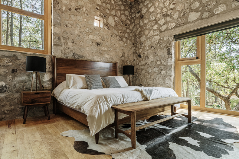 A Petraia House bedroom with stone walls and a cowhide rug designed by Argdl.