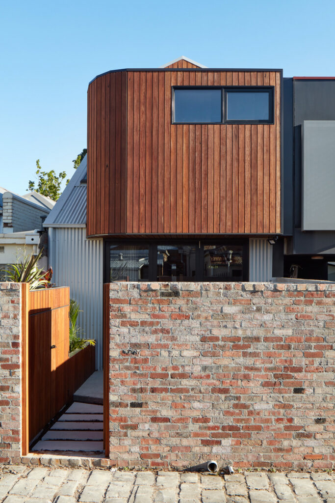 A modern house featuring a brick wall and wooden fence, inspired by "Through The Looking Glass" by Ben Callery Architects.