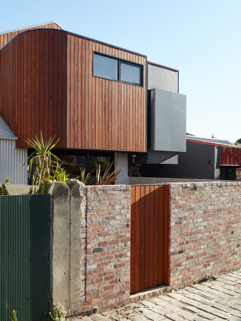A modern house with a wooden fence and a brick wall, inspired by "Through The Looking Glass" by Ben Callery Architects.