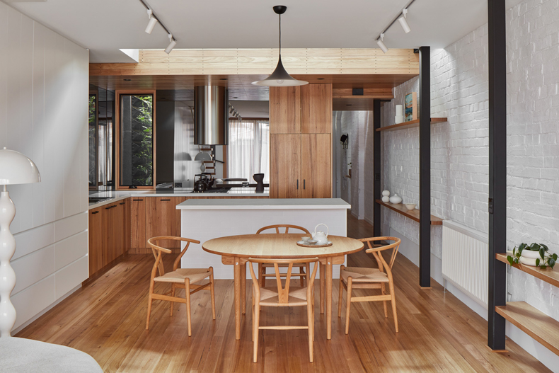 A kitchen and dining room designed by Ben Callery Architects, featuring wood floors and white walls.