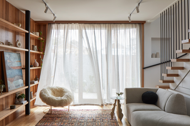 A living room featuring bookshelves and a couch designed through the looking glass by Ben Callery Architects.
