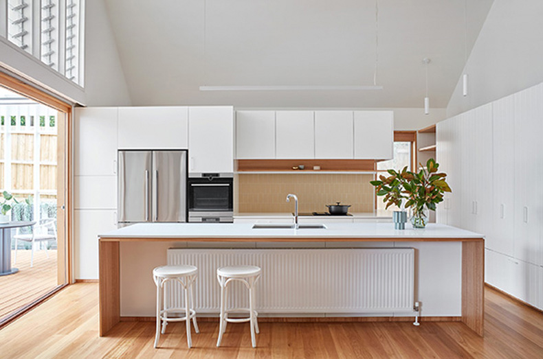 Twin Peaks House By Mihaly Slocombe featuring a white kitchen with wooden floors and stools.