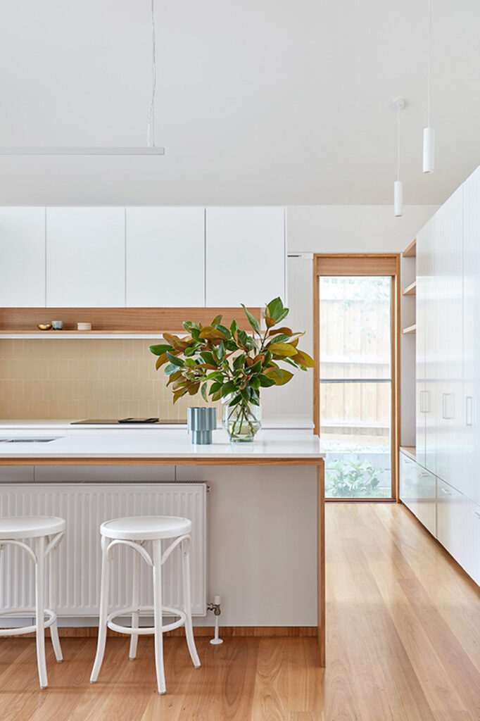 Twin Peaks House By Mihaly Slocombe features a modern kitchen with white cabinets and stools.