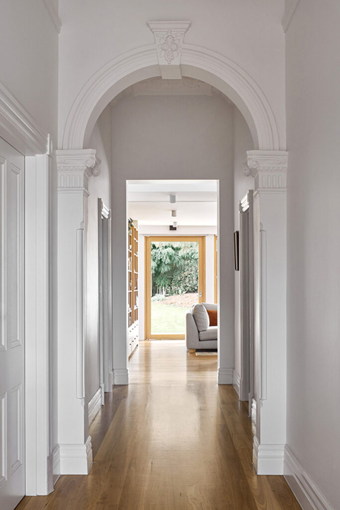 A Twin Peaks House hallway with a white archway and hardwood floors, designed by Mihaly Slocombe.