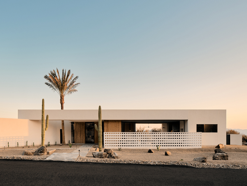 A white house in the desert with cactus and palm trees.
