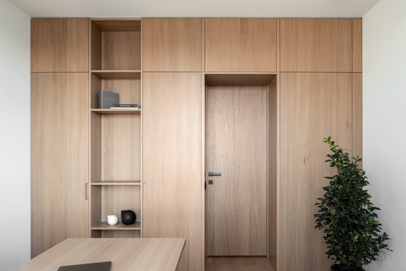 Zaricnyy Apartment By Kouple features a wooden office furnished with a desk and bookshelf.