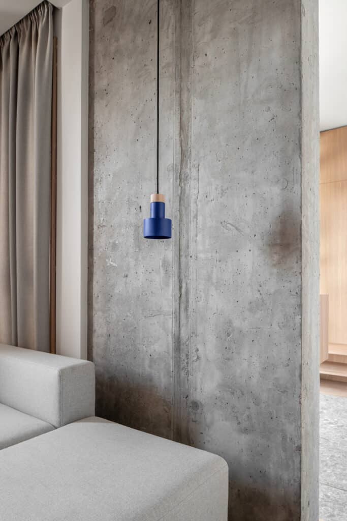 A living room with a concrete wall and a blue lamp in the Zaricnyy Apartment By Kouple.