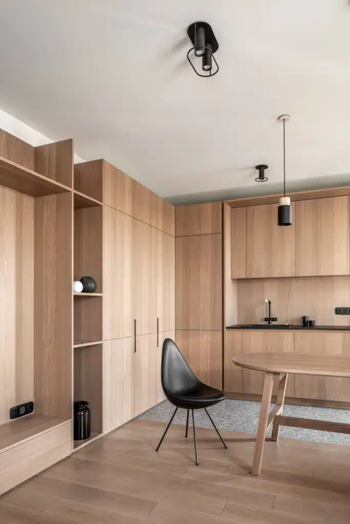 A kitchen with wooden cabinets and a black chair in the Zaricnyy Apartment By Kouple.