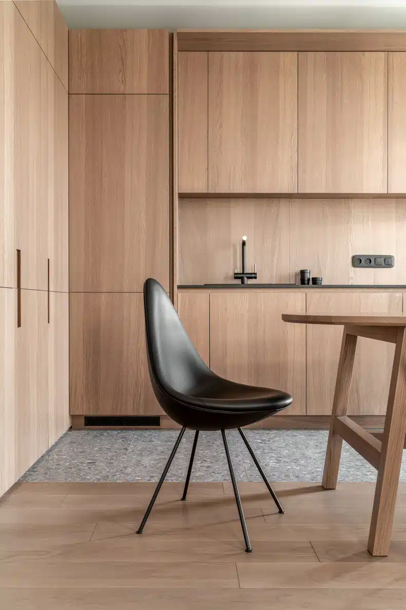 A modern kitchen with wooden cabinets and a black chair located in Zaricnyy Apartment By Kouple.