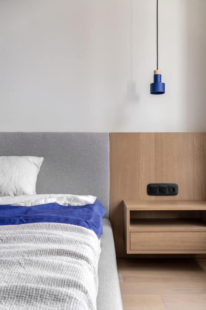 A Zaricnyy Apartment designed by Kouple featuring a bed with a blue comforter and a wooden nightstand.