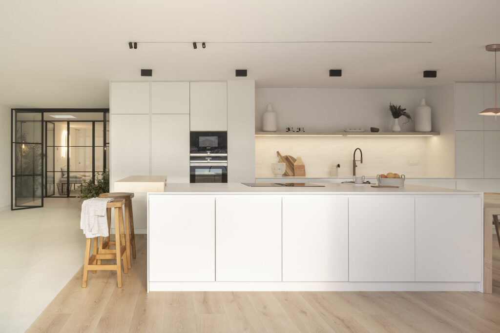 A modern kitchen with white cabinets and wooden floors in the Citric House By Susanna Cots Interior Design.