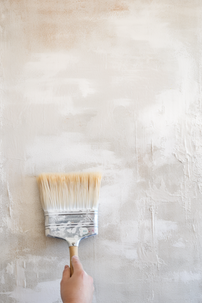 A person is painting a textured wall with a brush, creating visual interest and unique wall treatments.